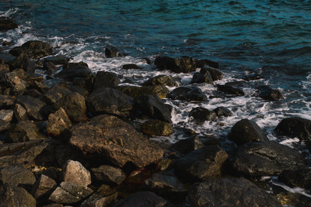 As the sun set over the ocean, waves crashed against the rock-strewn beach, painting a golden seascape and revealing a breathtaking landscape shaped by nature and sea.の写真素材