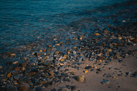 As the sun set over the ocean, waves crashed against the rock-strewn beach, painting a golden...