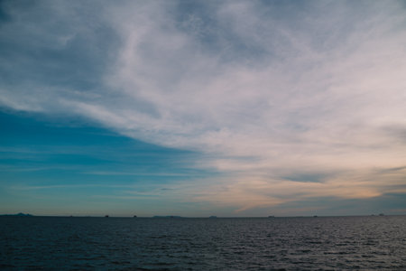 Blue water stretches to the horizon where sea and sky meet, clouds drifting gently as sunlight...