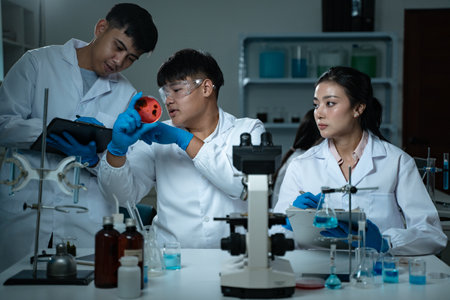 Three young scientists in lab coats working together in a laboratory examining a petri dish for...