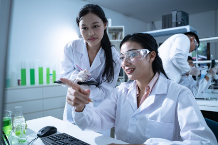 Young scientists analyze test tube results comparing them to computer data in a modern lab environment aiming to advance knowledge and scientific innovationの写真素材