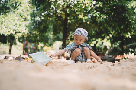 Children play happily in the summer garden, digging in the sand with toys, each person lost in the joy of childhood memories and carefree laughter under the sun.の写真素材