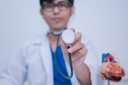 In the bustling hospital, the doctor used a stethoscope to listen to the patient's heartbeat during the exam, focusing on health care strategies to combat the disease in cardiology.の写真素材