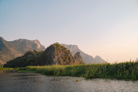 The mountain looms over a green landscape where a swamp meets a tranquil lake, water reflecting the sky, a single cloud drifting in peaceful, untouched nature.の写真素材