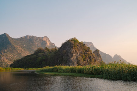 The mountain looms over a green landscape where a river meets a tranquil lake, water reflecting the...