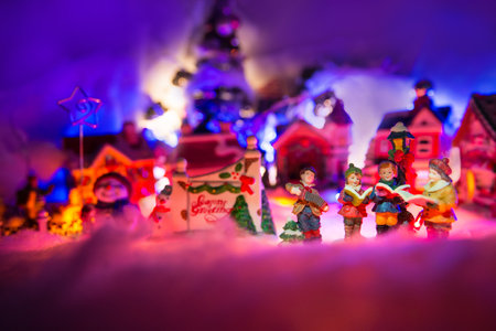 kid gospel choir singing next to Seasons greeting sign with  snowman and christmas village in the background. Fairytale miniature sceneryの写真素材