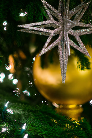 large star decorates on green christmas tree and lights blurred in the background. Holiday...