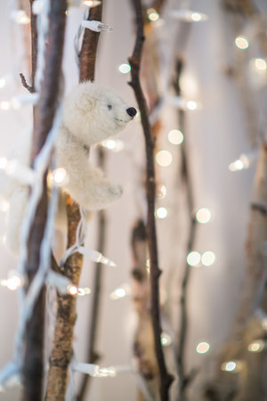 Christmas background. closeup white teddy bear clinches on birch branches blurred with Christmas lights wrap around.の写真素材