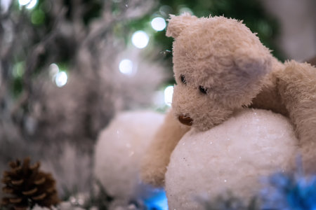 Beige teddy bear hugs snowballs with Christmas tree and lights blurred in the background.の写真素材