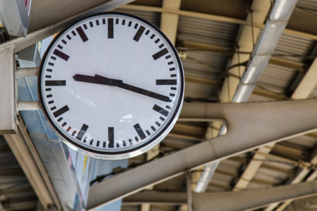 Public white roundcircular clock In a railway station perspective roof station train background blurの写真素材
