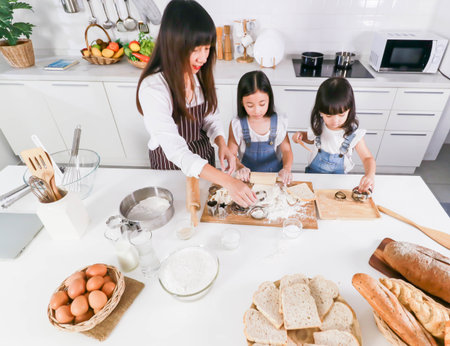 Asian mother and cute two daughter preparing the dough to make a cake in kitchen room at homeの写真素材