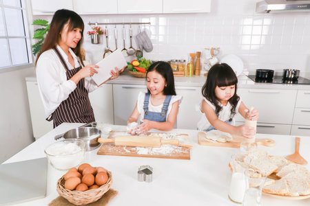 Asian happy family cooking together mom reading a book and two dauther preparing a bakeの写真素材