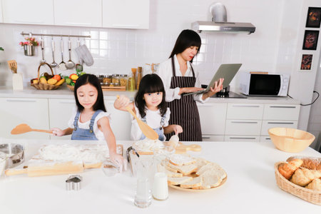 Close up two daughter make a bake and mother watch notebookの写真素材