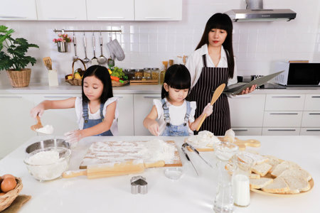 Mother looking ittle daughter and little sister make a bakeの写真素材