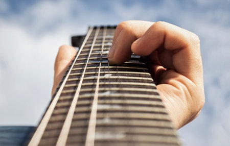 Male hand fingers in electric guitar fretboard with cloudy sky in the background. Focus on fingersの写真素材