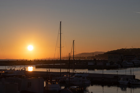 Dramatic sunset seen from a harbor with multiple sailboats and shipsの写真素材