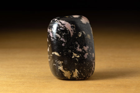Polished Rhodonite gemstone from South Africa over a wooden table