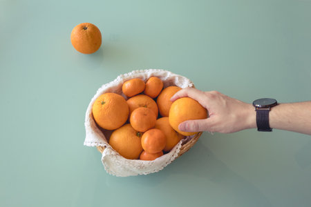 Hand holding an orange and showing it to the camera with other oranges in a ball on the background.の写真素材