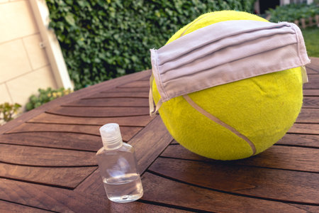 Tennis ball with a mask and disinfectant representing the sport in pandemic timeの写真素材