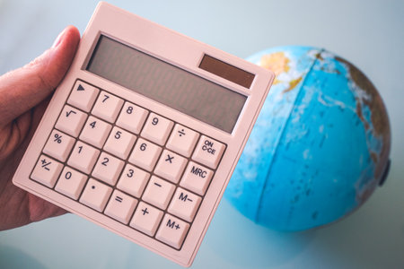 Hand holding a white calculator without any number on the screen perfect for putting anything there. And a world ball on the background.の写真素材