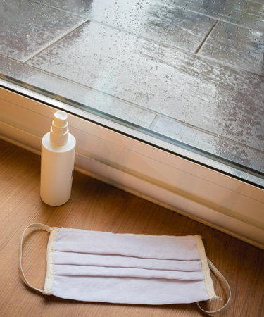Face mask and a disinfectant near the window in a rainy day at home.の写真素材