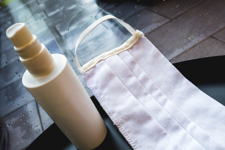 Face mask and a disinfectant near the window in a rainy day at home.の写真素材