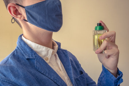 Business elegant man in a blue suit using perfume with face mask. Symbolizing the new normality of using mask, he can be preparing for a meeting or a date.の写真素材