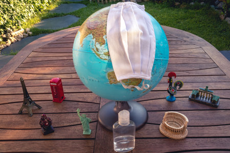 Earth globe with different famous monuments like eiffel tower, coliseum etc on a wooden table, also a face mask and a disinfectant. related to globlal pandemic theme and virus .の写真素材