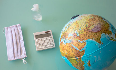 Photo of a mask, disinfectant, calculator and earth with on a crystal tableの写真素材