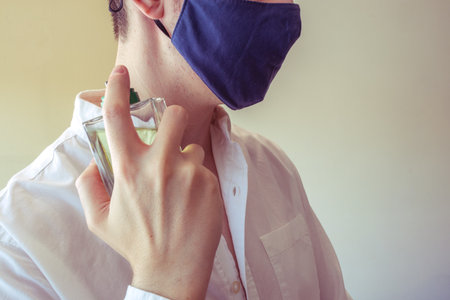 Elegant man using perfume with face mask. Symbolizing the new normality of using mask, he can be preparing for a date or going out.の写真素材