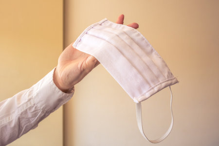 Hand holding a white face mask made by fabric. Meaning the usage of the mask for prevention, pandemic cases or medical.の写真素材