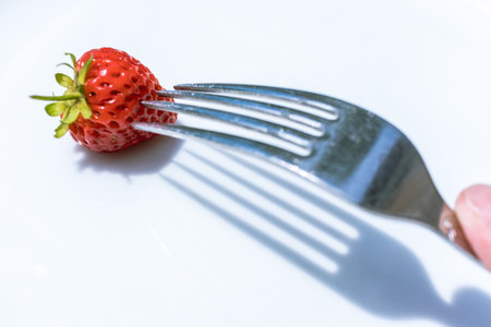 Isolated strawberry with red color on a white background put it on a forkの写真素材