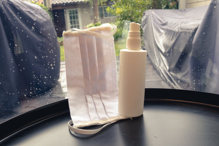 Face mask and a disinfectant near the window in a rainy day at home.の写真素材