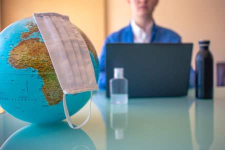 Earth with a face mask and Business man on a desk working with a mask on the background blurred, working on a computer.の写真素材