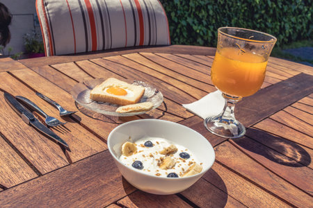 Beautiful breakfast in a garden with a wooden table. Breakfast made of sandwich egg, fruit yogurt and orange juice.の写真素材