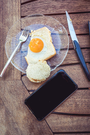 Business breakfast. Egg with bread on a wooden table with a phoneの写真素材