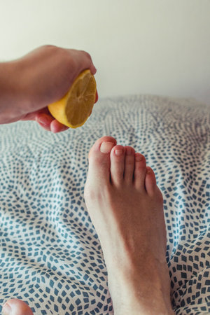 Hand holding a yellow lemon with a small young feet on a bed.の写真素材