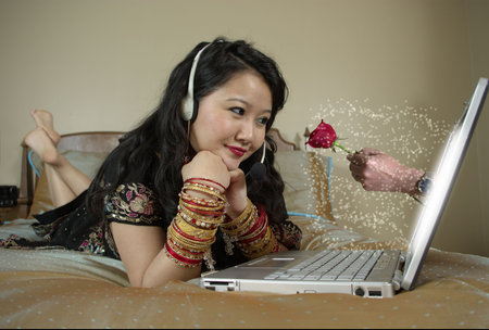 girl lying on bed wearing a sari, talking online to a friend, imagining him giving her a flower の写真素材