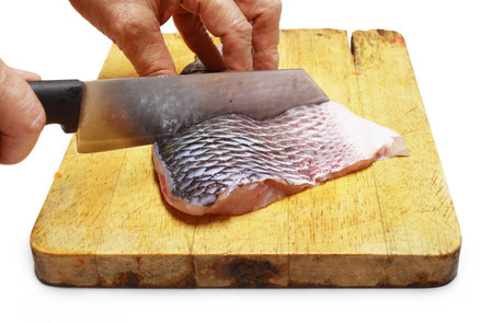 Chef is chopping fresh raw fish fillet of sea bass on chopping blockの写真素材