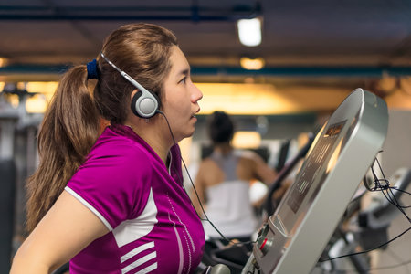 Fat Asian woman is exercising hard on a treadmill to get a good workout in fitness center room