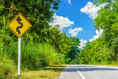 Yellow winding road sign at roadside in countryside of Thailandの写真素材