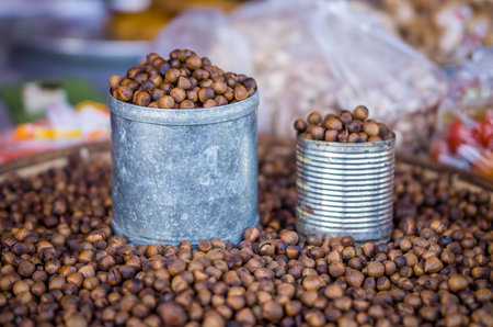 Tin cans and heap of roasted Lithocarpus seeds for retail sale in Thailand marketの写真素材