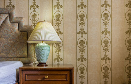 Vintage interior with jade stone desk lamp, bed, wooden nightstand and wallpaper in bedroomの写真素材