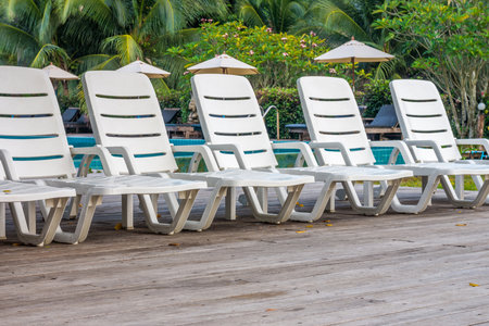 Line of white plastic sunbeds on wooden deck in garden. The outdoor recreation in luxury hotel.