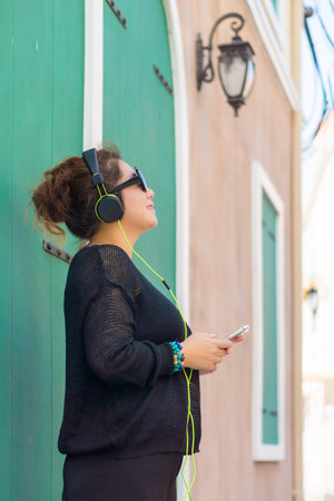 Pretty Asian lady is listening to music from mobile phone. She is smiling and standing in vintage...