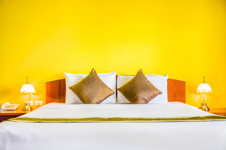 Interior decoration of romantic plain yellow bedroom. It consists of bed, white pillows, gold cushions, retro lamps and telephone.の写真素材