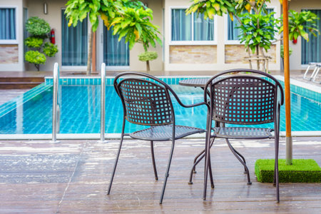Metal table and chairs on wooden decks at the side of swimming pool. For relaxation and recreation in hotel resort.の写真素材