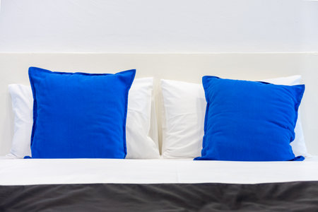 Two white pillows and blue cushions on bed in a bedroom. The plain design of romantic light pale room.の写真素材