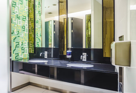 New modern restroom with touch-free automatic sensor faucets. It consists of new mirror, ceramic washbasins, granite countertop, liquid soap and toilet paper roll holder.の写真素材