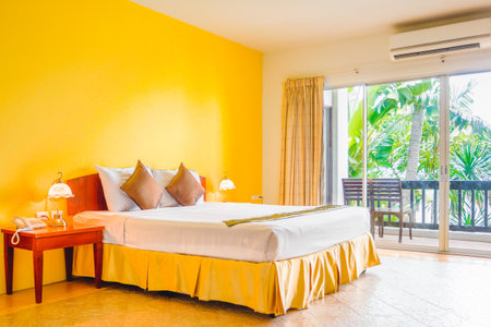 Interior decoration of romantic plain yellow bedroom with balcony. It consists of bed, white pillows, gold cushions, vintage lamps, telephone and side tables.の写真素材